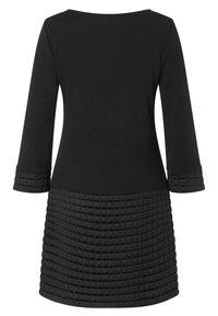 Svart klänning med en slät överdel med trekvartslånga ärmar och en strukturerad, vadderad nederdel som framhäver visuell kontrast och detalj.