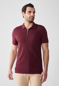 Kort burgunder polo skjorte med glidelås krage, laget av glatt stoff. Fitted design med korte ermer, kombinert med lyse bukser.
