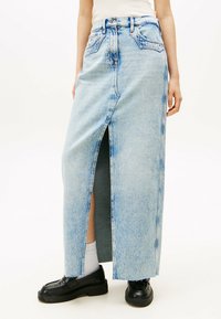 Lichtblauwe denim maxirok met een voorkant split, hoge taille en zichtbare stiksels. Gepaard met zwarte schoenen en witte sokken.