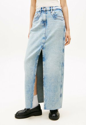Jupe maxi en denim bleu clair avec une fente à l'avant, taille haute et couture visible. Associée à des chaussures noires et des chaussettes blanches.