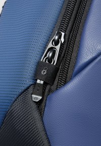 Tessuto blu strutturato e pelle liscia si combinano con cerniere nere. Una chiusura di sicurezza è presente sulla linguetta della cerniera per una protezione aggiuntiva.