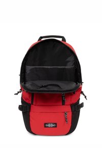 Zaino in tessuto rosso con un'ampia apertura nera con zip, tasca interna in rete, spallacci laterali regolabili e tasca anteriore in rete nera.