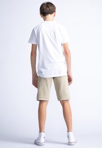 Witte katoenen t-shirt, beige shorts en witte high-top sneakers. De shorts hebben een casual snit, met een omgeslagen zoom en zakken.