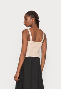 Top cropped bege com alças finas, apresentando uma textura franzida nas costas, combinado com uma saia preta para contraste.