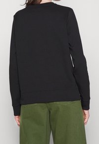 Felpa nera con collo tondo e maniche lunghe, abbinata a pantaloni verdi a vestibilità comoda, mostrata da dietro. Texture liscia.