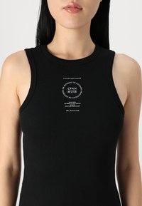 Čierny rebrovaný tielko s okrúhlym výstrihom a širokými prieramkami, s centrálnym bielym logom na prednej strane. Tkanina vyzerá pružne a priliehavo.