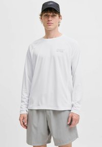 Wit sportshirt met lange mouwen van textuurstof en het 'CNZ'-logo op de borst, gecombineerd met lichtgrijze shorts.