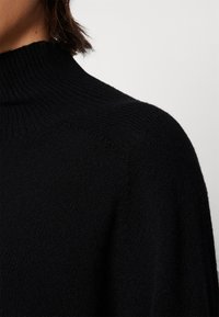 Schwarzer Rollkragenpullover mit geripptem Kragen, weichem Material und lässiger Passform. Verfügt über dezente Nähte an den Schultern.