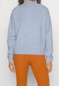 Ljusblå turtlenecktröja med mjuk textur och lös passform. Ribbad nederkant och ärmslut. Matchad med orange ribbade byxor.
