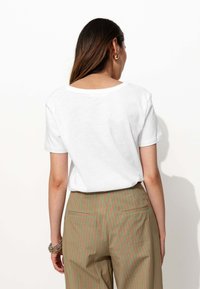 T-shirt blanc à manches courtes avec un col rond, associé à un pantalon vert avec des rayures rouges verticales et des poches au dos.