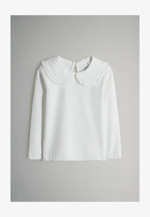 Biała bluzka z długim rękawem o prążkowanej teksturze, z okrągłym kołnierzem z falbankami i zapięciem na guziki z tyłu.