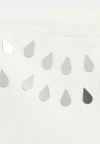 Tissu blanc avec une rangée de clous en métal argenté en forme de goutte d'eau disposés en ligne courbe près d'une couture.