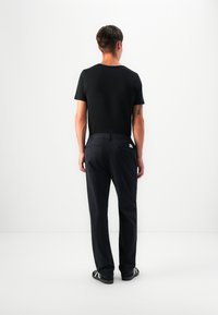 T-shirt nera in cotone e pantaloni blu navy con vestibilità slim. I pantaloni presentano una tasca posteriore con un'etichetta bianca e una texture sottile.