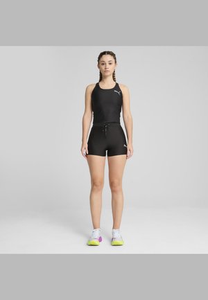 Crna sportska majica s dizajnom racerback, u kombinaciji s crnim hlačama koje imaju remen za podešavanje. Uključuje šarene tenisice s detaljima.