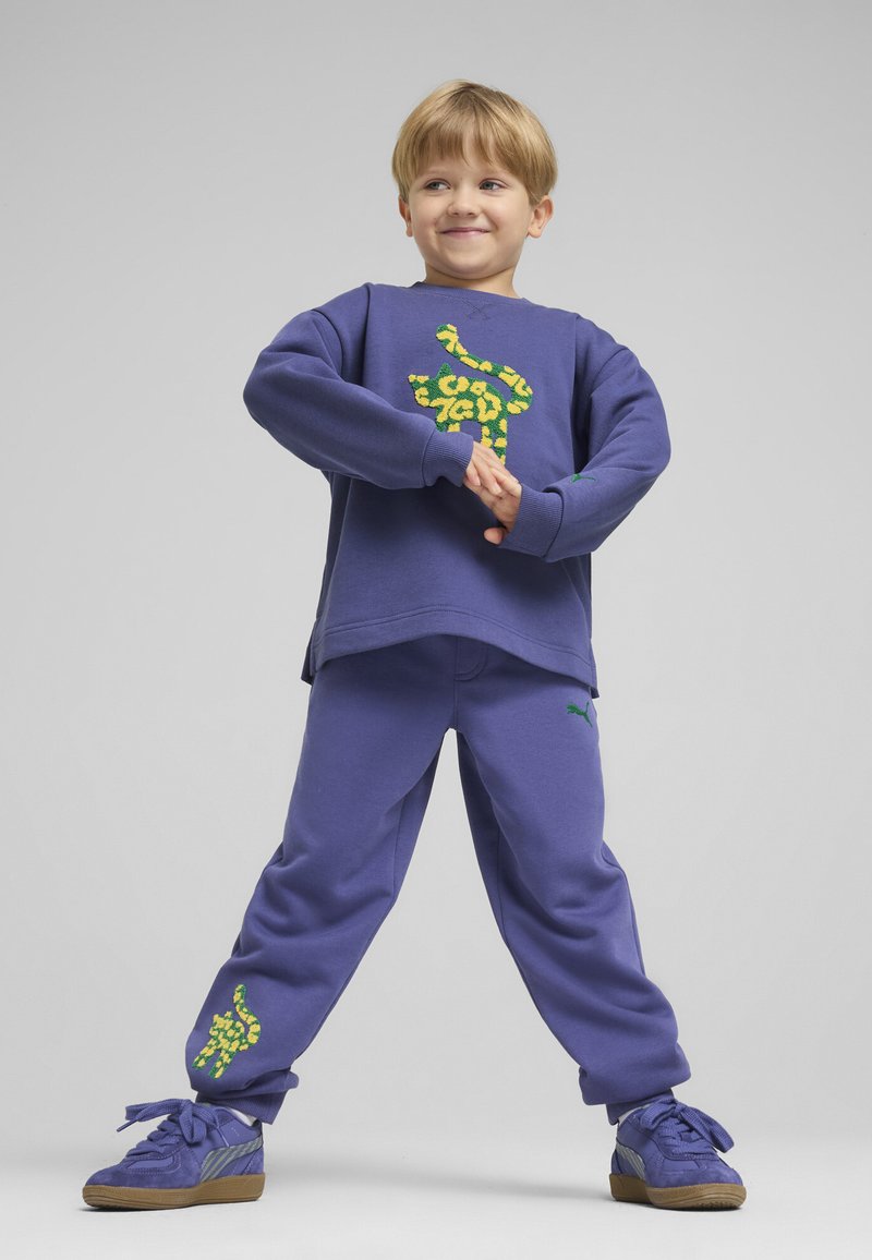 Sudadera morada con diseño de estampado de leopardo verde y pantalones de chándal morados a juego. Presenta puños y un logo de Puma en los pantalones.