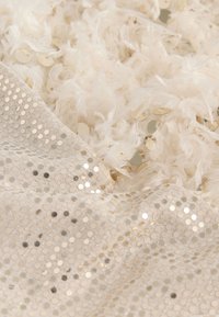 White fabric with a fluffy texture and light feathers, embellished with gold sequins and a mesh panel featuring round cutouts.