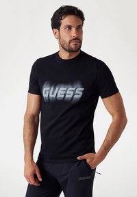 Zwarte katoen t-shirt met een groot, vervaagd grijs "GUESS" logo op de voorkant. Korte mouwen en een klassiek ronde hals ontwerp.