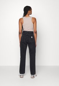 Sorte høyhøyde jeans med store baklommer og en liten logo-lapp, kombinert med en tettsittende lys brun tanktop. Hvit og svart joggesko.