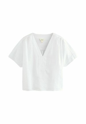 Blouse blanche à manches courtes avec col en V, coupe ample et légers fronces aux épaules, présentée sur fond blanc.