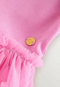 Roza pletenina s nagubanim tilom in z zlatim okroglim gumbom kot detajlom. Gladka tekstura z nabranim dizajnom na robu.