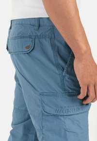 Light blue cargo shorts with multiple pockets, stitched detailing, and "MADE FOR DAILY ADVENTURES" embossed on the leg. Soft texture.
