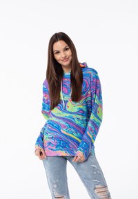 Sudadera colorida con un patrón que mezcla azul, rosa, verde y amarillo en espiral. Cuenta con capucha y mangas largas, combinada con jeans claros desgastados.