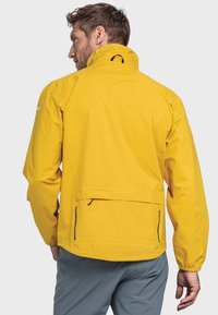 Gelbe wasserdichte Jacke mit hohem Kragen, elastischen Bündchen und Seiten Taschen. Das Design verfügt über einen Rückenschlitz für Belüftung und Beweglichkeit.