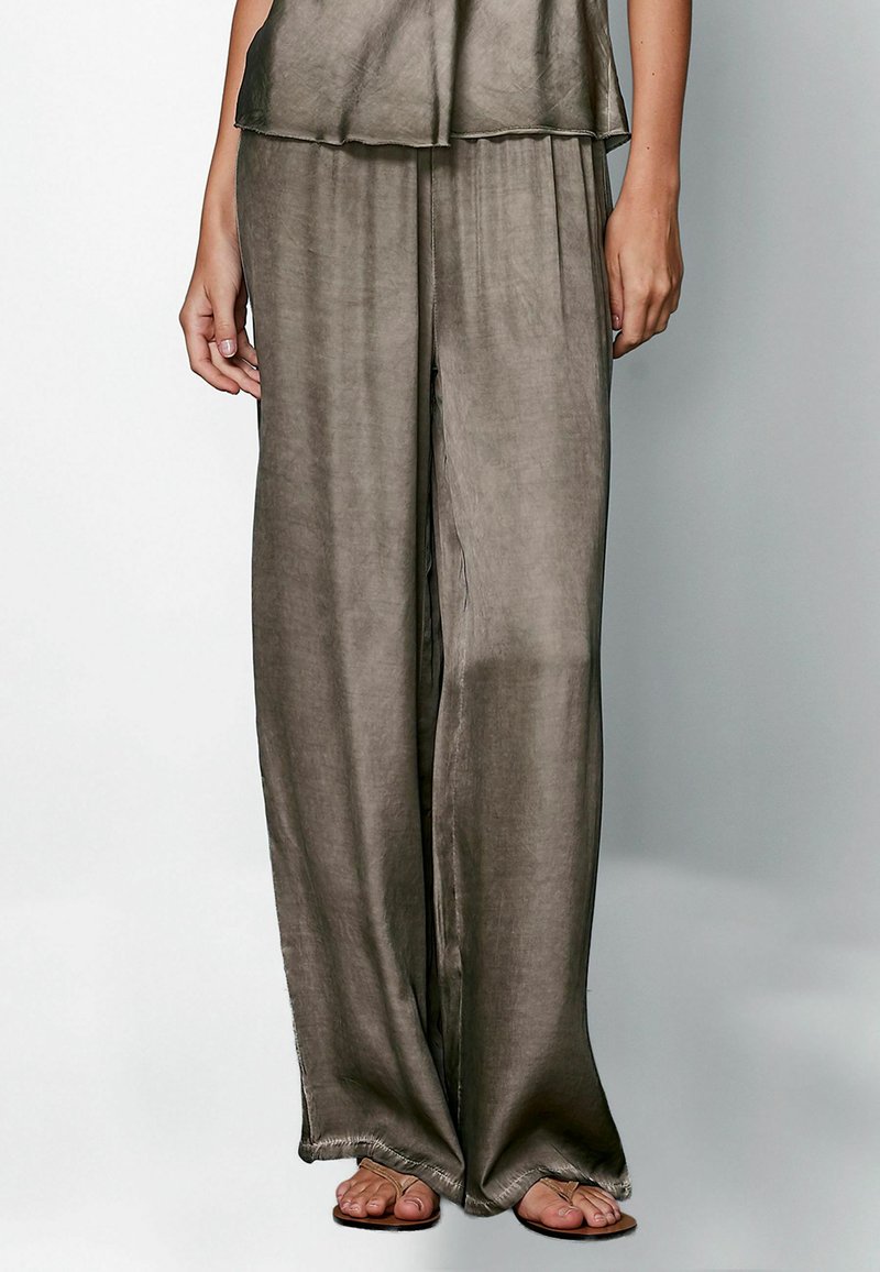 Pantalones de pierna ancha en verde oliva, confeccionados con un material suave y sedoso, que presentan una cintura con cordón y acentos de dobladillo sin coser. Combinados con sandalias sencillas.