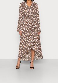 Vestido maxi floral con mangas largas, escote en V y cintura anudada, en tonos de marrón, blanco y naranja con una silueta fluida. Tacones negros.
