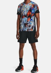 Camiseta deportiva de manga corta con un patrón abstracto en azul, naranja y rojo, combinada con pantalones cortos negros y zapatillas negras y naranjas.