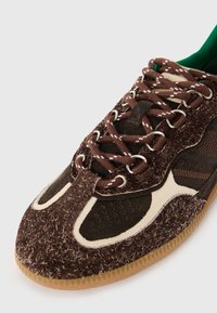 Sneakers marroni con una combinazione di texture morbide e pelose, dotati di lacci marroni, sezioni perforate e una suola in gomma. Accento di dettagli crema.