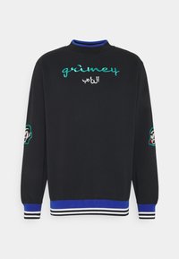 Sweat-shirt noir à col haut, avec texte brodé turquoise et blanc "grimey" et inscription en arabe, ainsi que des accents à motifs sur les manches.