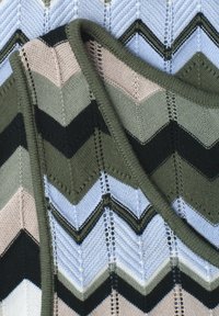 Tissu tricoté avec motif chevron aux couleurs alternées beige, vert olive, noir et bleu clair avec détail de bord plié.