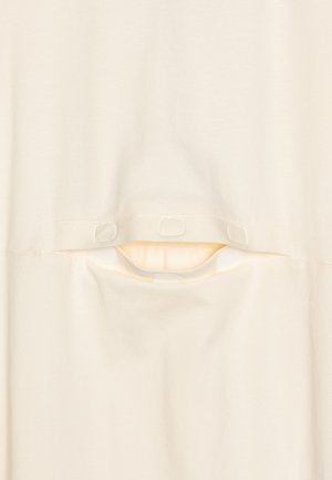 Prenda de color crema con una textura suave, un pequeño corte con cierres de botones y un diseño simple y minimalista.