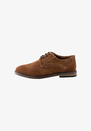 Chaussure brogue pour homme en daim marron avec lacets noirs, perforations en forme d'aile et talon empilé sur fond blanc.