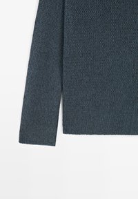 Maglione a maniche lunghe grigio scuro lavorato a maglia, mostrato dalla metà del busto al polso su sfondo bianco.