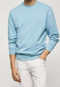 Felpa leggera blu con scollo rotondo realizzata in tessuto morbido, con maniche lunghe, polsini a coste e una vestibilità rilassata. Abbinata a pantaloni bianchi.
