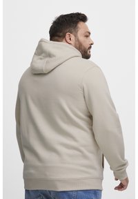 Sudadera beige con cremallera y capucha con cordón, bolsillo laterales y puños acanalados. Tejido suave con una textura lisa, exhibida desde la parte de atrás.