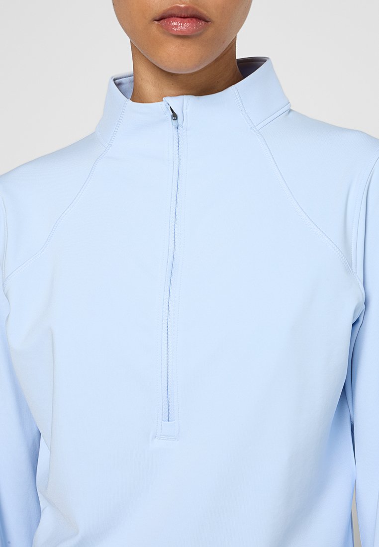 Haut bleu clair à manches longues avec un col zippé mi-hauteur. Fabriqué en tissu lisse et extensible, avec des coutures discrètes, conçu pour un ajustement près du corps.