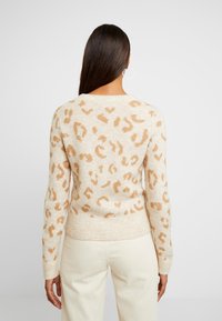 Suéter beige con estampado de leopardo en marrón claro, textura de punto, mangas largas y dobladillo acanalado, combinado con pantalones de color claro.