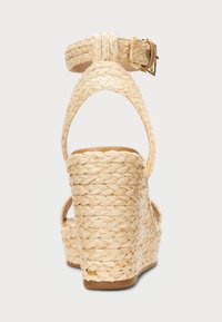 Sandalové kliny s tkaným slaměným zvrškom, hnedou vnútornou časťou, nastaviteľným remienkom okolo členka a textúrovaným podpätkom.