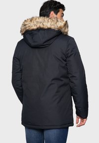 Svart parkajacka med en pälsfodrad huva, med en slät yta och rak skärning, visad bakifrån med blå jeans.