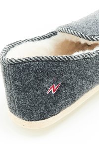 Pantoufle grise avec une doublure douce beige. Présente une bordure rayée noire et blanche ainsi qu'un petit logo rouge sur le côté. Semelle plate.