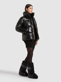 Sort pufferjakke med høj krave og blank finish, kombineret med sorte vinterstøvler til knæet med snørebånd og teksturerede detaljer.