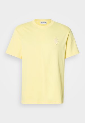 T-shirt gialla in cotone con maniche corte, scollo a girocollo e un sottile dettaglio ricamato a forma di diamante sul petto.