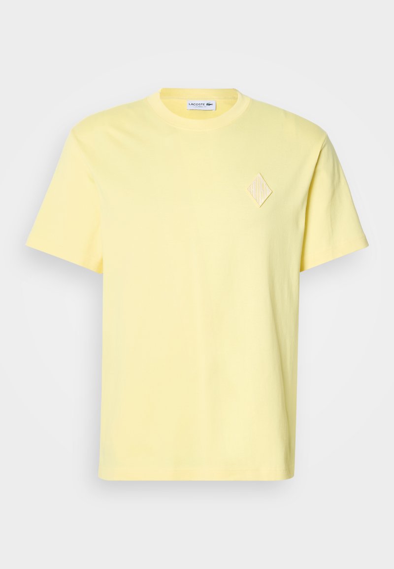 T-shirt gialla in cotone con maniche corte, scollo a girocollo e un sottile dettaglio ricamato a forma di diamante sul petto.