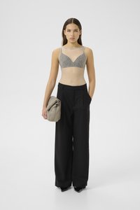 Bralette in pizzo grigio, trasparente con motivo testurizzato, abbinato a pantaloni neri a gamba larga con vita alta; tiene una borsa morbida e piegata di un grigio chiaro.