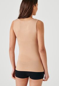 Top senza maniche beige aderente con spalline larghe e superficie liscia, abbinato a pantaloni corto neri. Design semplice senza motivi o dettagli.