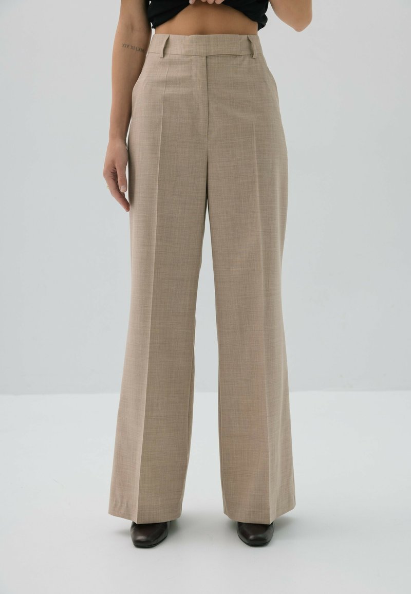Beżowe spodnie o szerokich nogawkach z teksturowanej tkaniny, wysoki stan i fałdy z przodu. Charakteryzują się prostym designem i dopasowanym krojem.