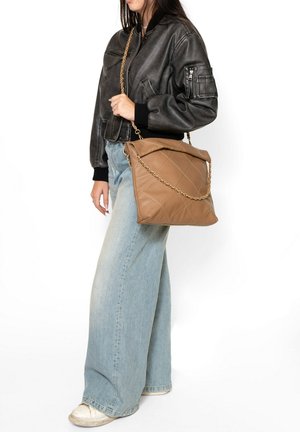 Borsa a spalla in pelle tan con motivo trapuntato e tracolla in oro, dotata di un bordo pieghevole. Abbinata a jeans in denim blu larghi e una giacca bomber nera.